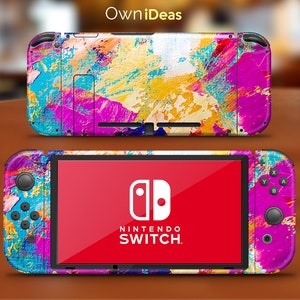 May include: A colorful abstract design Nintendo Switch console skin with a pink, yellow, blue, and white paint splatter pattern. The skin is applied to the front and back of the console, as well as the Joy-Con controllers.