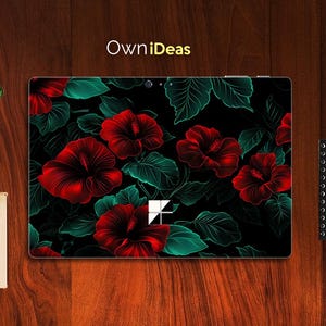 Puede incluir: Una piel para portátil con fondo oscuro y un diseño floral con flores de hibisco rojas y hojas verdes. La piel tiene un recorte para la cámara del portátil y un logotipo que dice "OwnIdeas".