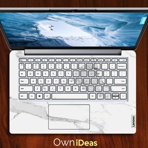 May include: A white laptop with a marble design skin. The laptop has a white keyboard with black keys and a black touchpad. The screen is showing a picture of a snowy mountain range.