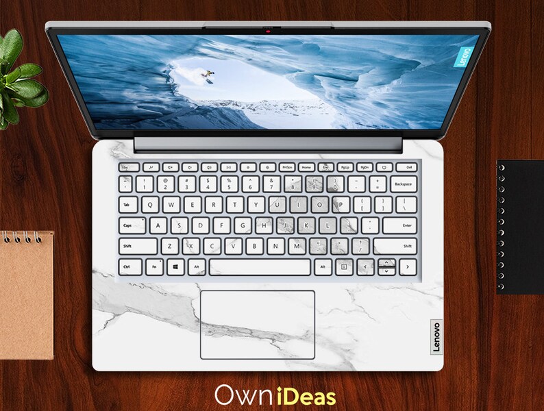 May include: A white laptop with a marble design skin. The laptop has a white keyboard with black keys and a black touchpad. The screen is showing a picture of a snowy mountain range.