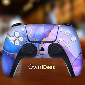 Puede incluir: Un mando de PlayStation 5 de color morado y azul con un diseño de mármol dorado. El mando tiene el logotipo de OwnIdeas en la parte delantera.