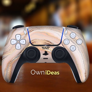 May include: A custom-designed Playstation 5 controller with a beige and gold marble pattern. The controller features the standard Playstation buttons and a black and white logo.
