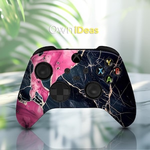Op de afbeelding: Een zwarte en roze Xbox-controller met een marmerpatroon en gouden accenten. De controller heeft een zwart-witte D-pad en zwarte knoppen.