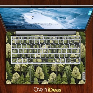 May include: A laptop computer with a green and white forest design on the keyboard and trackpad. The laptop is closed and the screen is showing a blue and white image of a snowy mountain.