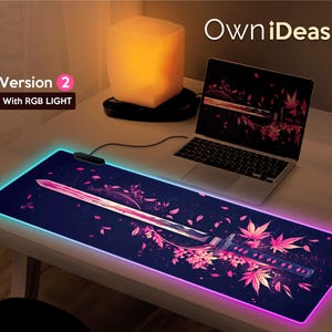 Könnte beinhalten: Eine schwarze und violette Gaming-Mausmatte mit einem leuchtend rosa und blauen Rand. Die Mausmatte zeigt ein stilisiertes Bild eines Schwertes und von Blumen. Der Text "OwnIdeas" und "Version 2 with RGB LIGHT" ist im Bild sichtbar.
