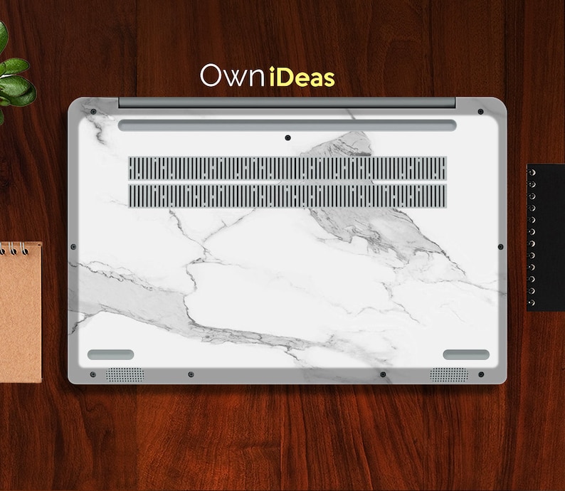 May include: A white laptop with a marble design on the lid. The laptop has a silver trim and a black keyboard. The laptop is closed and sitting on a wooden surface.