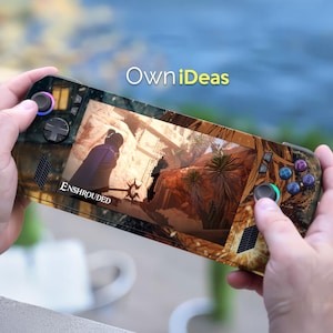 Könnte beinhalten: Eine Handheld-Spielkonsole mit einem Wüsten-Design wird vor einem verschwommenen Hintergrund gehalten. Der Bildschirm zeigt eine Videospielszenen mit dem Wort "ENSHROUDED". Die Konsole hat mehrere Tasten und Joysticks, und der Text "OwniIdeas" ist sichtbar.
