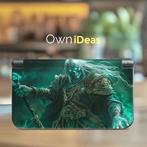 Puede incluir: Una piel verde y negra para Nintendo 3DS XL con un guerrero esquelético con ojos azules brillantes que sostiene un bastón. El guerrero está rodeado de una niebla verde.
