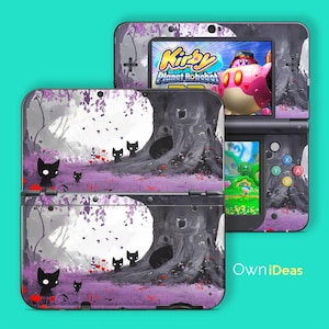 Puede incluir: Una consola Nintendo 3DS con una piel personalizada que presenta una escena de bosque caprichosa con siluetas de gatos negros, un árbol grande y acentos morados. La pantalla muestra el juego "Kirby Planet Robobot". La consola es negra y gris.