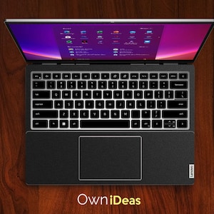 May include: A black laptop computer with a silver lid is open and displaying a desktop screen with various icons. The laptop is on a wooden surface with a brown notebook and a black notebook to the side. The text "Own iDeas" is printed in yellow below the laptop.