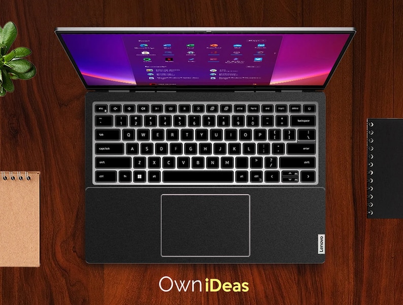 May include: A black laptop computer with a silver lid is open and displaying a desktop screen with various icons. The laptop is on a wooden surface with a brown notebook and a black notebook to the side. The text "Own iDeas" is printed in yellow below the laptop.