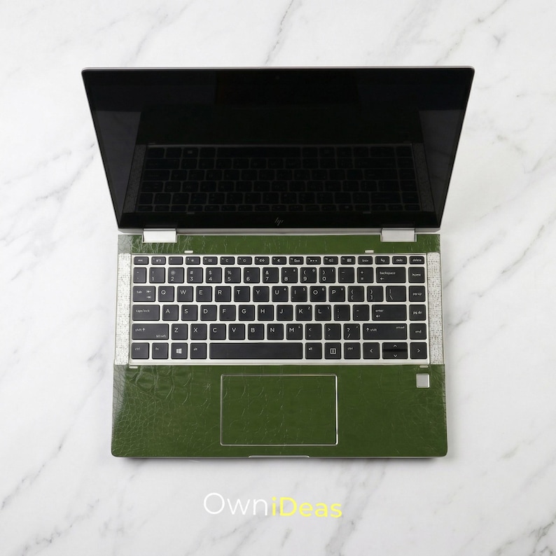 May include: An open laptop with a green textured skin. The keyboard has white keys with black lettering. The screen is black and reflects the keyboard. The laptop is on a white marble surface. The text "OwniIdeas" is at the bottom.