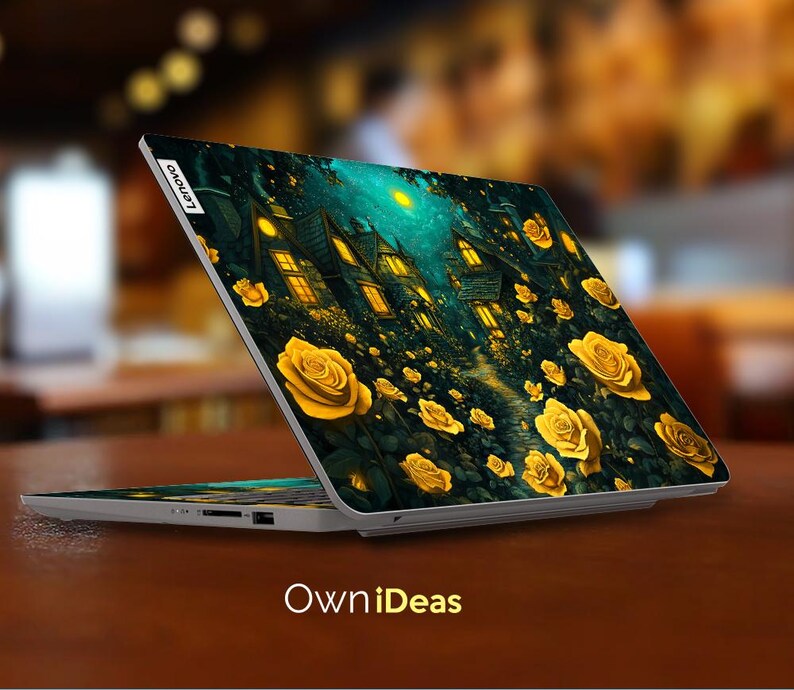 Puede incluir: Un ordenador port&aacute;til con un fondo azul oscuro y verde que presenta una escena caprichosa de casas y rosas amarillas. El port&aacute;til tiene el logotipo de Lenovo en la tapa.