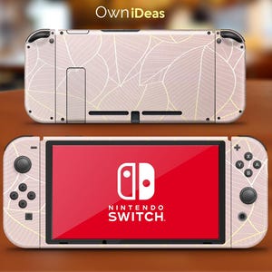 Puede incluir: Una consola Nintendo Switch rosa con un diseño de patrón de hojas blancas. La consola está cerrada y el logotipo de Nintendo Switch es visible en la pantalla.