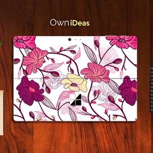 Puede incluir: Una piel de portátil blanca con un diseño floral con flores rosas, moradas y amarillas. El diseño incluye líneas blancas finas y hojas. La piel tiene el texto "OwnIdeas" en la parte superior.