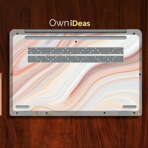 May include: A laptop with a white marble design on the lid. The design features swirls of white, brown, and orange. The laptop has a silver trim and a black vent.