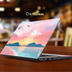 Op de afbeelding: Lenovo laptop met een aangepaste skin met een zonsondergang boven water. Het ontwerp bevat roze, oranje en blauwe tinten, met bergen en vogels in silhouet. De laptop staat open op een bruin oppervlak.