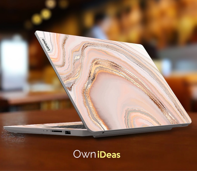 Op de afbeelding: Een laptop met een wit en gouden marmerontwerp op de deksel. De laptop is gesloten en het Lenovo-logo is zichtbaar op de deksel.