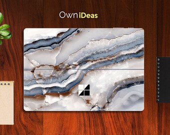 May include: A laptop skin with a white, blue, and brown marble pattern. The skin has a cut-out for the laptop's camera and a logo that says "OwnIdeas".
