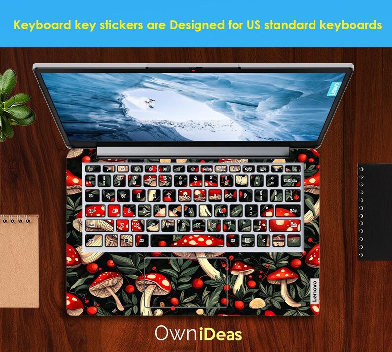 May include: Laptop with a keyboard skin featuring red and white mushrooms, green leaves, and red berries on a black background. The keyboard keys are black and white. The screen displays a landscape. Text at the top says, "Keyboard key stickers are Designed for US standard keyboards."