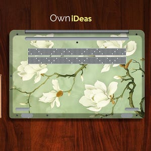 May include: A laptop skin with a floral design featuring white magnolia blossoms on a light green background. The design includes a branch with leaves and buds. The skin has the text "OwnIdeas" printed on the top.