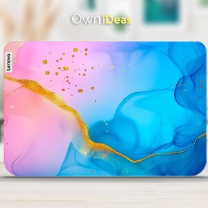 Op de afbeelding: Een laptop-skin met een abstract ontwerp in blauw en roze met gouden accenten. Het ontwerp heeft draaiende lijnen en gouden stippen. De skin heeft het woord "Lenovo" aan de linkerkant gedrukt.