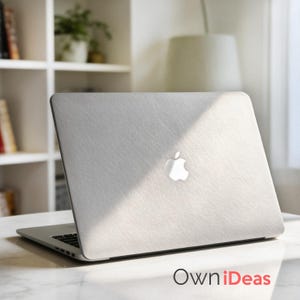 K&ouml;nnte beinhalten: Ein silberner Laptop mit einer strukturierten, hellgrauen Abdeckung mit dem Apple-Logo. Der Laptop ist auf einer wei&szlig;en Marmoroberfl&auml;che ge&ouml;ffnet. Der Text "OwniDeas" ist unten rechts sichtbar.