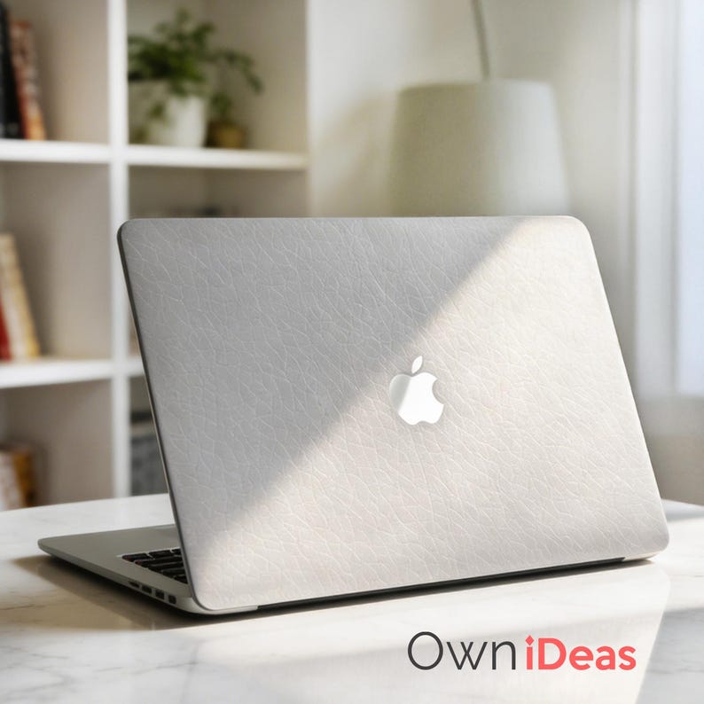 K&ouml;nnte beinhalten: Ein silberner Laptop mit einer strukturierten, hellgrauen Abdeckung mit dem Apple-Logo. Der Laptop ist auf einer wei&szlig;en Marmoroberfl&auml;che ge&ouml;ffnet. Der Text "OwniDeas" ist unten rechts sichtbar.
