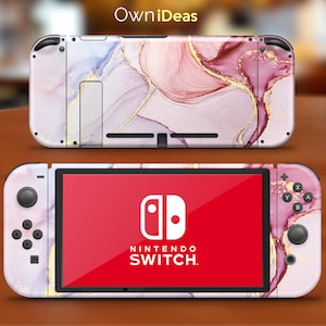 Könnte beinhalten: Eine rosa und violette Nintendo Switch Konsole mit Marmormuster und goldenen Akzenten. Die Konsole wird mit geöffnetem Bildschirm und dem Nintendo Switch Logo angezeigt.