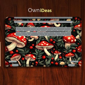 May include: Laptop skin featuring a vibrant pattern of red and white mushrooms with green leaves and red berries on a black background. The text "OwniDeas" is in yellow. The design covers the top of the laptop.