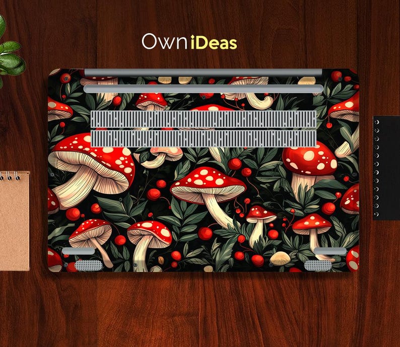 May include: Laptop skin featuring a vibrant pattern of red and white mushrooms with green leaves and red berries on a black background. The text "OwniDeas" is in yellow. The design covers the top of the laptop.