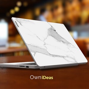 May include: A white laptop with a marble design on the lid. The laptop is closed and the Lenovo logo is visible on the lid. The laptop is sitting on a wooden table. The text "OwnIdeas" is visible below the laptop.