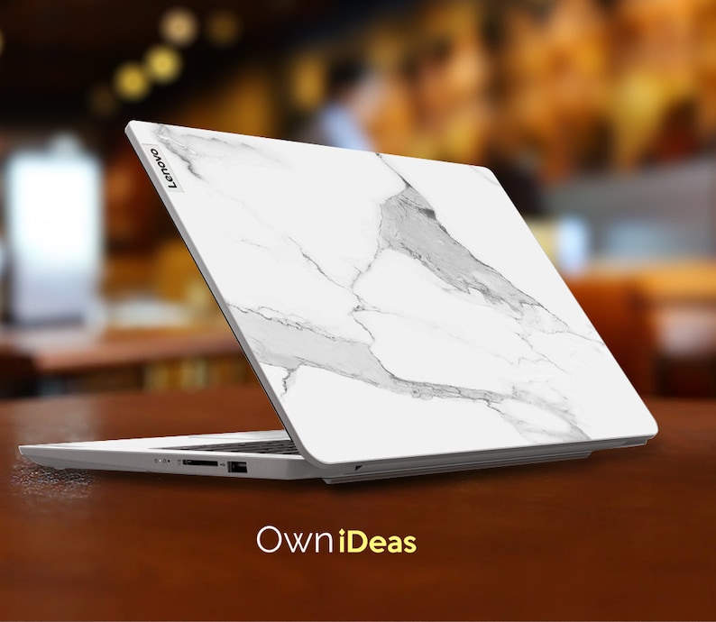 May include: A white laptop with a marble design on the lid. The laptop is closed and the Lenovo logo is visible on the lid. The laptop is sitting on a wooden table. The text "OwnIdeas" is visible below the laptop.