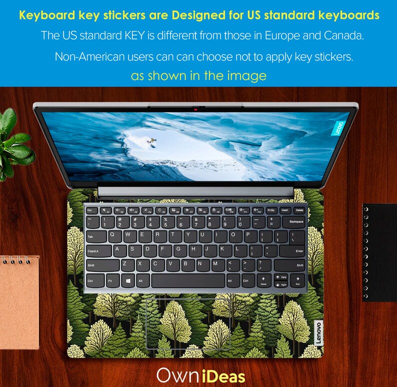May include: A laptop computer with a green forest design keyboard sticker. The sticker features a repeating pattern of pine trees with green and yellow leaves. The laptop is on a wooden surface.
