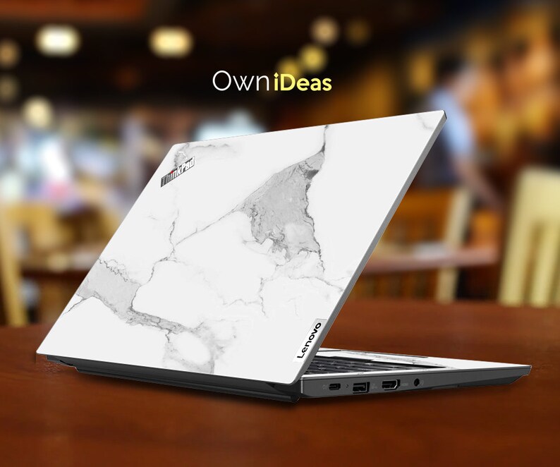 May include: A white laptop with a marble design on the lid. The laptop is open and the screen is facing away from the viewer. The laptop is sitting on a wooden table. The text "OwnIdeas" is visible in the background.