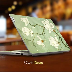 May include: A laptop computer with a green and white floral design on the lid. The design features white magnolia flowers and branches on a light green background. The laptop is open and the screen is off. The Lenovo logo is visible on the lid.