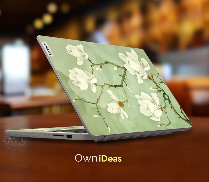 May include: A laptop computer with a green and white floral design on the lid. The design features white magnolia flowers and branches on a light green background. The laptop is open and the screen is off. The Lenovo logo is visible on the lid.