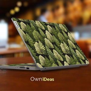 May include: A silver laptop with a green and white leafy pattern on the lid. The laptop is closed and the Lenovo logo is visible on the lid. The laptop is sitting on a wooden surface.