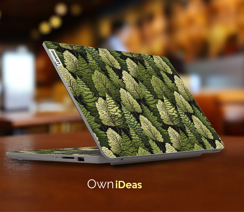 May include: A silver laptop with a green and white leafy pattern on the lid. The laptop is closed and the Lenovo logo is visible on the lid. The laptop is sitting on a wooden surface.