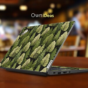 May include: A black laptop with a green and yellow leafy pattern on the lid. The laptop is open and the screen is facing away from the camera. The laptop is sitting on a wooden table. The text "OwnIdeas" is visible at the top of the image.