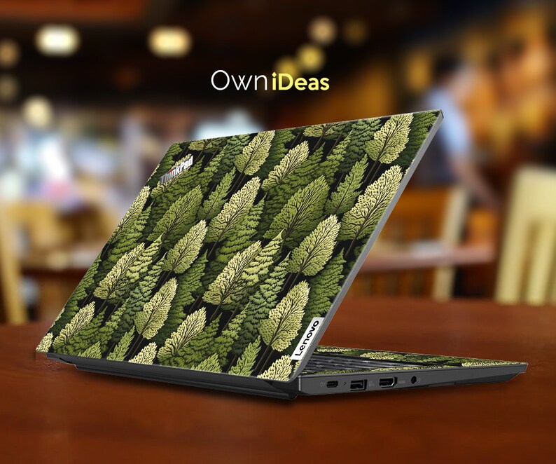 May include: A black laptop with a green and yellow leafy pattern on the lid. The laptop is open and the screen is facing away from the camera. The laptop is sitting on a wooden table. The text "OwnIdeas" is visible at the top of the image.
