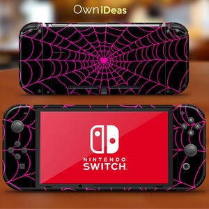 Könnte beinhalten: Eine schwarze Nintendo Switch Konsole mit einem pinkfarbenen Spinnennetz-Design. Die Konsole hat einen roten Bildschirm mit dem Nintendo Switch Logo und Text.