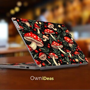 May include: A laptop with a custom cover featuring a vibrant pattern of red and white mushrooms with white stems, green leaves, and red berries on a black background. The laptop is open on a brown surface, with the text "OwniDeas" at the bottom.