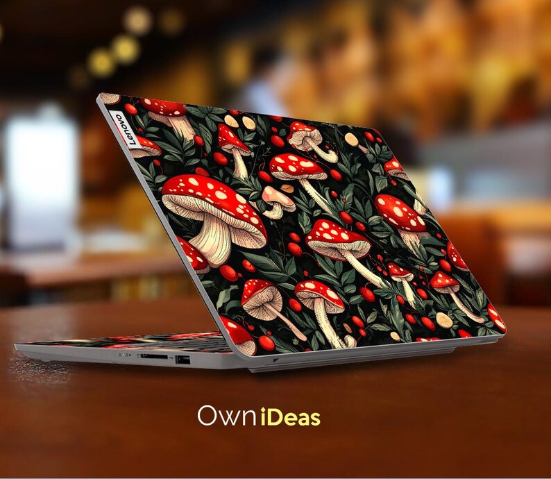 May include: A laptop with a custom cover featuring a vibrant pattern of red and white mushrooms with white stems, green leaves, and red berries on a black background. The laptop is open on a brown surface, with the text "OwniDeas" at the bottom.