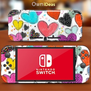 Peut inclure: Une console Nintendo Switch avec une peau personnalisée ornée de cœurs. La peau présente un fond blanc avec des cœurs colorés de différentes tailles et couleurs, notamment rouge, bleu, jaune et noir. Le logo Nintendo Switch est visible à l'écran.