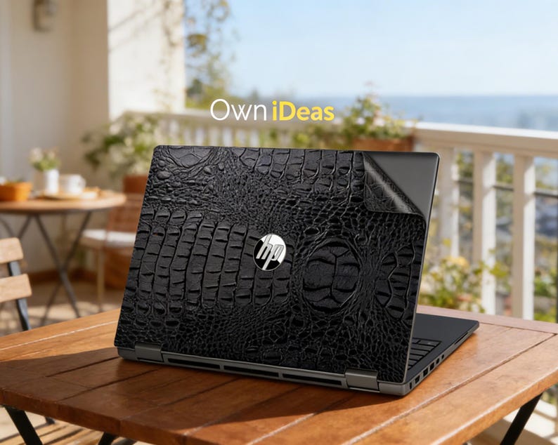 May include: Black laptop skin with a crocodile leather texture, featuring the HP logo. The laptop is placed on a wooden table outdoors, with the text "Own iDeas" in the background.