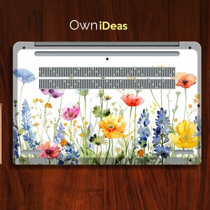 Puede incluir: Un port&aacute;til blanco con un dise&ntilde;o floral en la parte posterior. El dise&ntilde;o presenta flores de acuarela en tonos de azul, rosa, amarillo y rojo. Las flores est&aacute;n dispuestas en una fila horizontal a trav&eacute;s de la parte posterior del port&aacute;til.