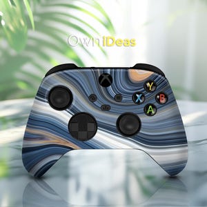 Op de afbeelding: Een zwarte Xbox-controller met een blauwe en witte swirl-patroon skin. De controller heeft de standaard Xbox-knoppen, waaronder A, B, X, Y en een directionele pad.