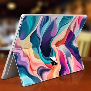 Puede incluir: Un portátil blanco con un diseño abstracto colorido en la tapa. El diseño presenta remolinos de azul, morado, rosa y amarillo.