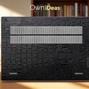 May include: Black laptop skin with a crocodile texture. The skin has two silver-colored vent strips and the text "OwniIdeas" in the upper left corner. The laptop skin is on a wooden surface.